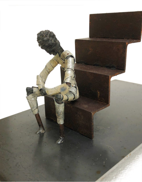 Steel sculpture of a figure seated at the base of a flight of stairs. Titled "Stoop". By Tony O'Keefe. Artist from Queenstown, New Zealand.